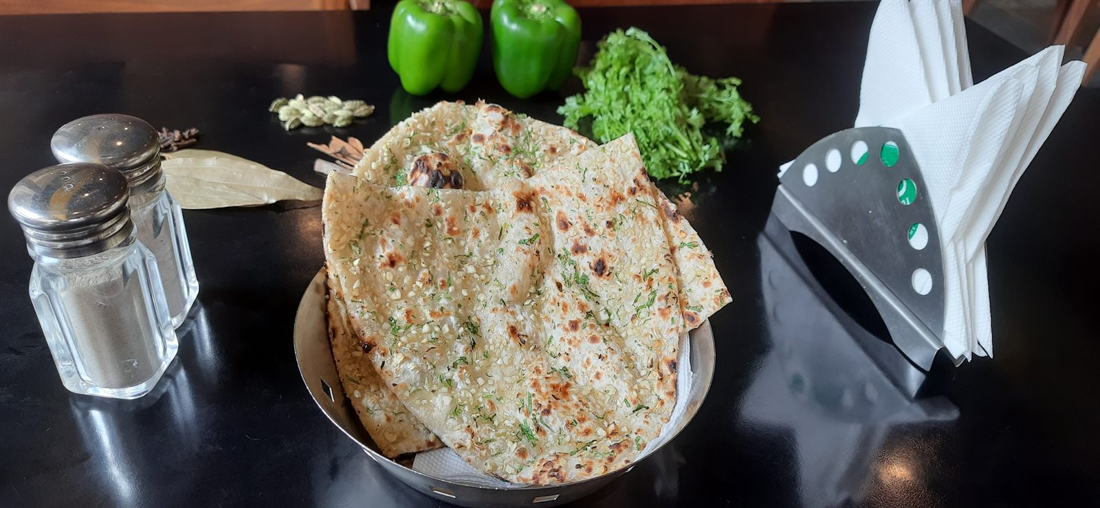 Basket of garlic butter naan with coriander and green peppers behind
