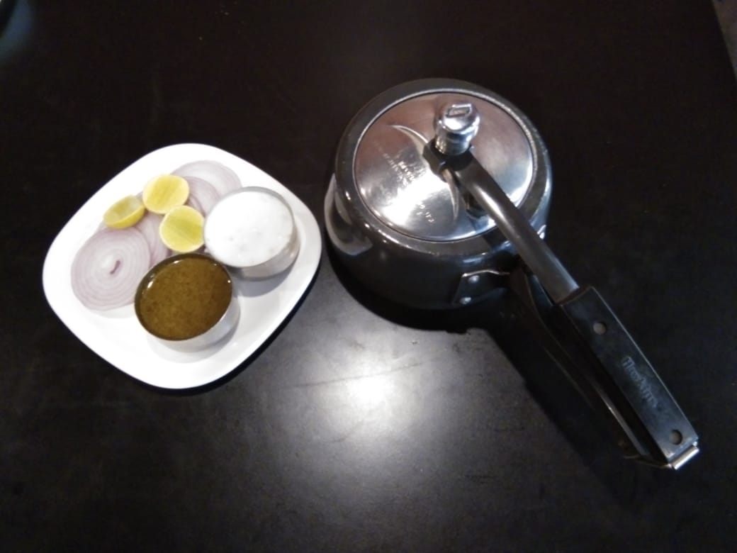 Steel pressure cooker served at the table with onion, lemon and raita