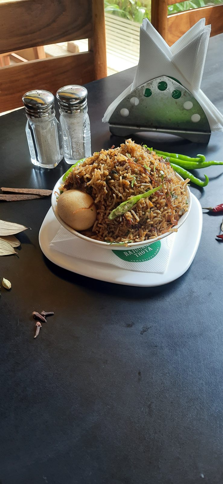 Bowl of egg biryani with a whole egg, garnished with fried onions and green chilli