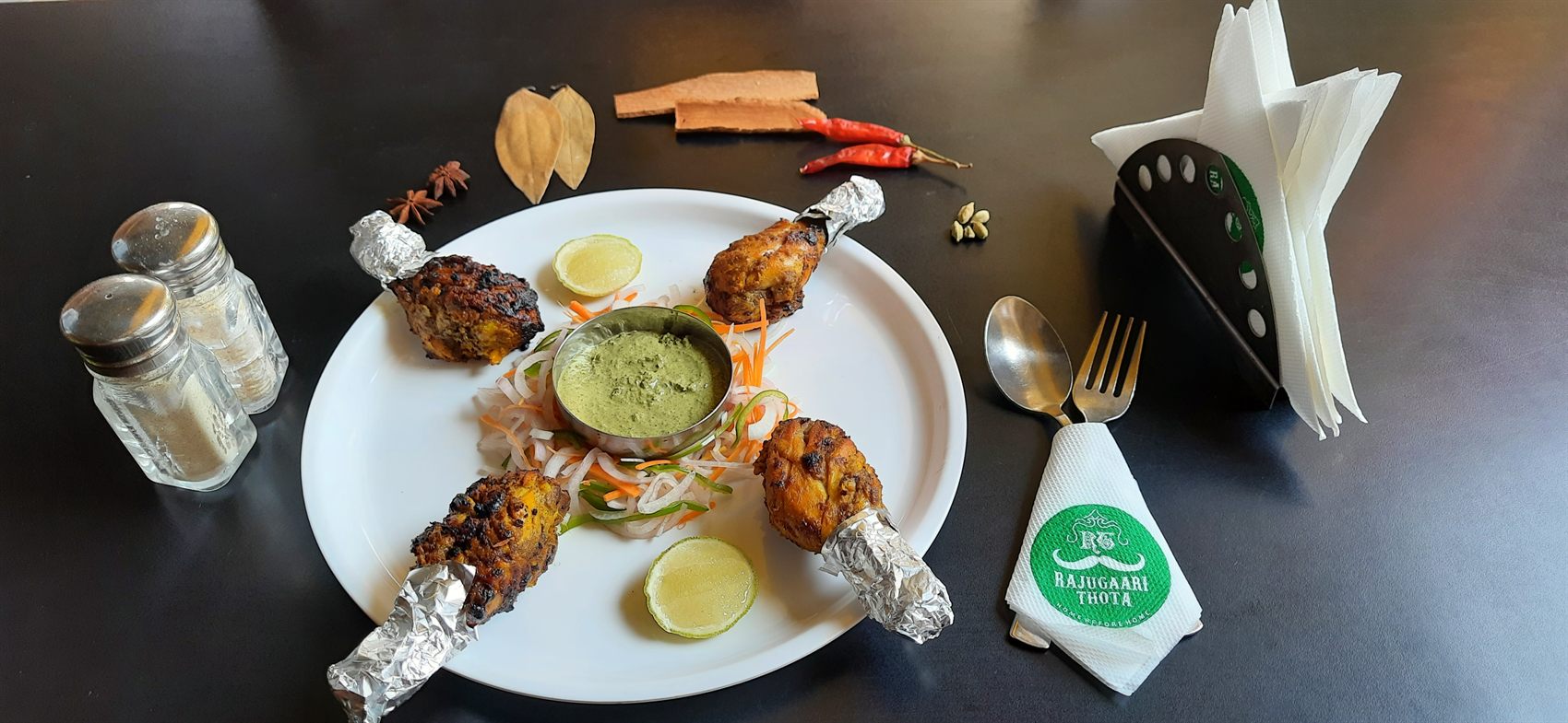 Four tangdi kebab drumsticks in foil wraps arranged around mint chutney